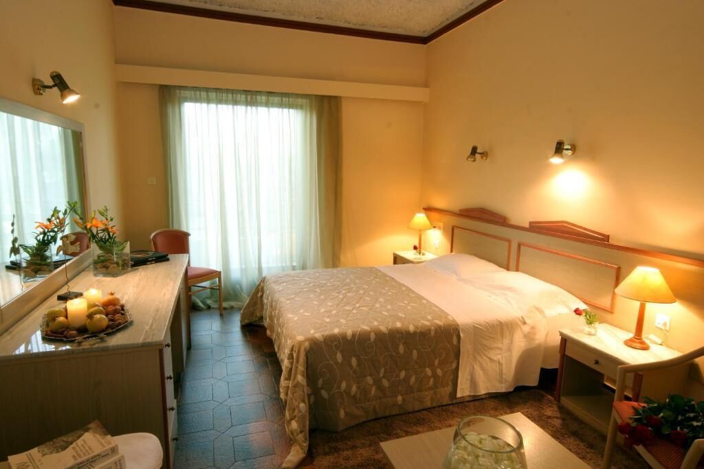 A hotel room with a bed, bedside tables, a desk with a mirror, a chair, and a window with curtains.