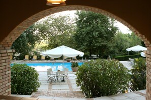 Un área de piscina al aire libre con un arco de ladrillo, sillas de descanso y sombrillas.