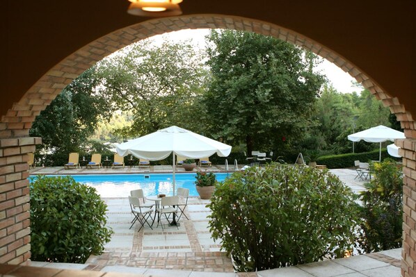 Un área de piscina al aire libre con un arco de ladrillo, sillas de descanso y sombrillas.