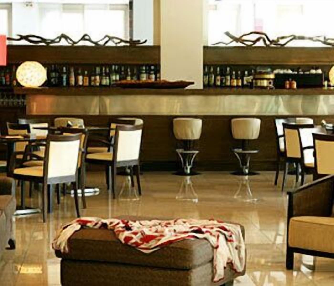 Uma área de bar com diversas opções de assento, incluindo banquetas e cadeiras, e uma variedade de garrafas nas prateleiras.