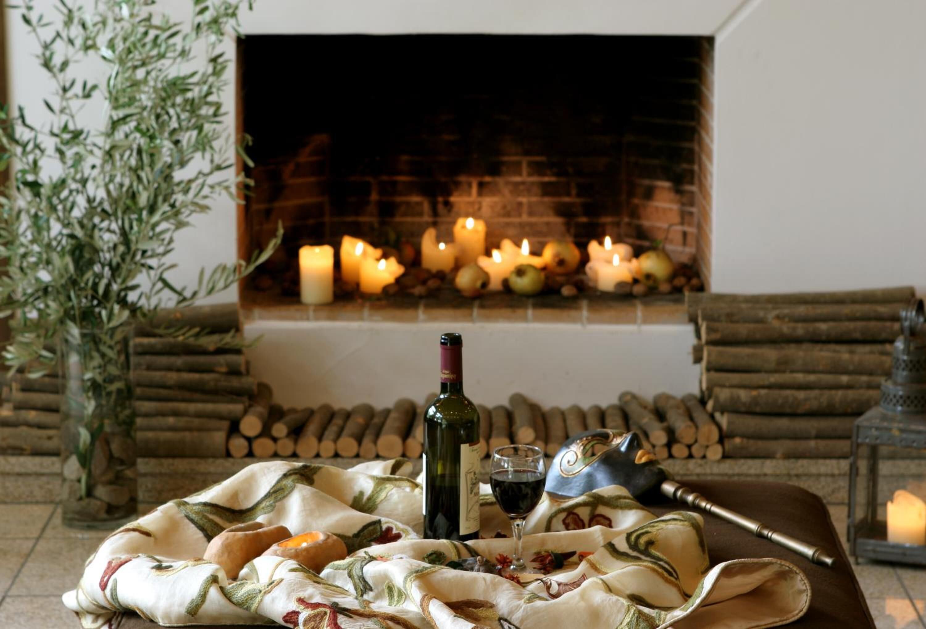 A cozy room with a fireplace, candles, a bottle of wine, and a blanket.