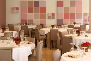Un restaurante con mesas redondas, sillas color beige y manteles blancos.