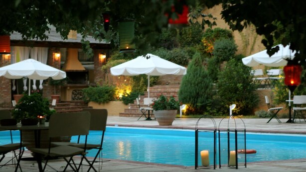 An outdoor pool area with seating and umbrellas, surrounded by greenery and brick walls. - Antonios (Archaia Olympia)