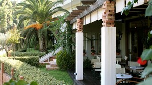 A hotel with a covered outdoor seating area, a palm tree, and a brick staircase. - Antonios (Archaia Olympia)