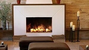 A modern living room with a fireplace, two ottomans, a side table, and decorative vases. - Antonios (Archaia Olympia)