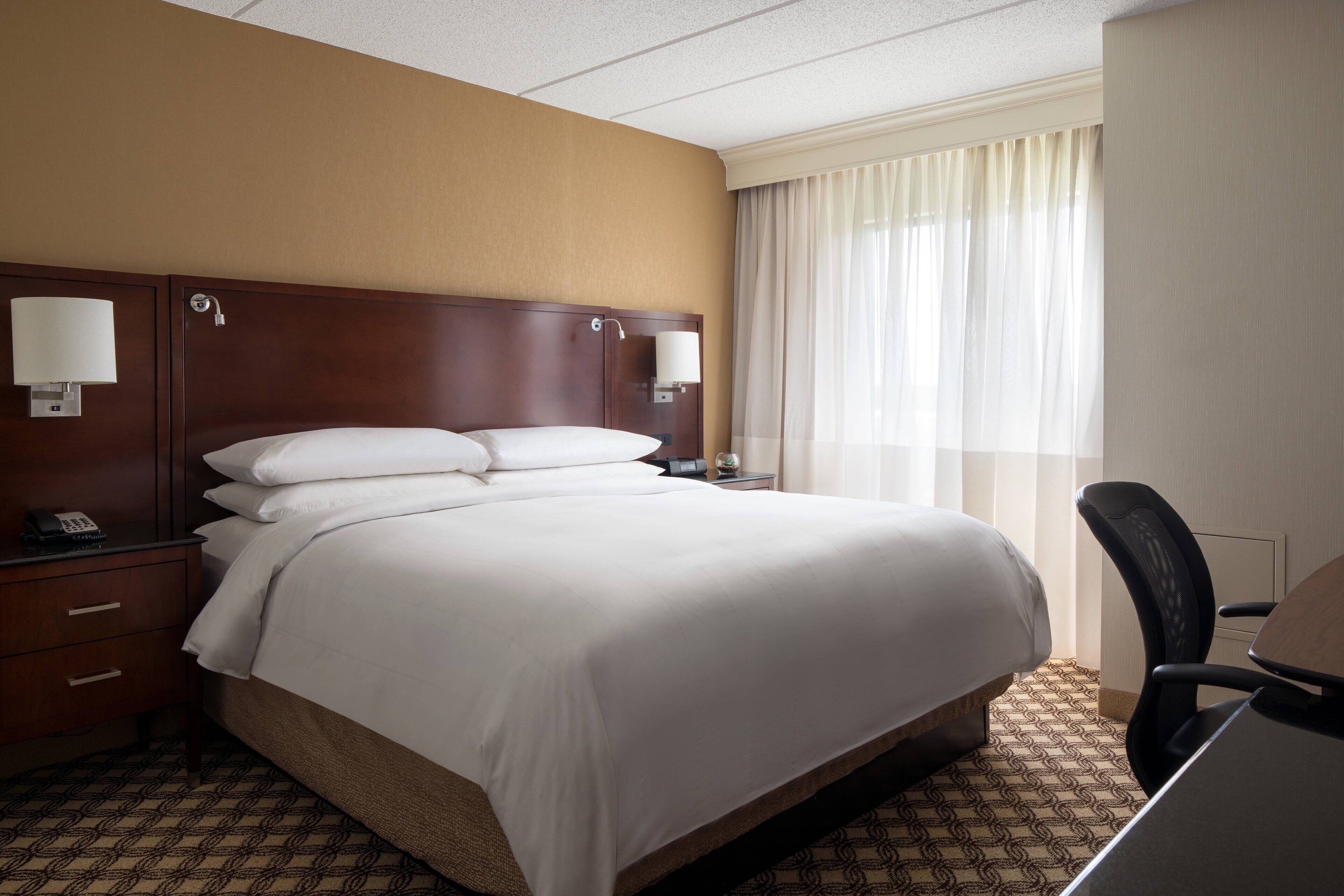 A hotel room with a large bed, two bedside tables with lamps, a desk, and a chair.