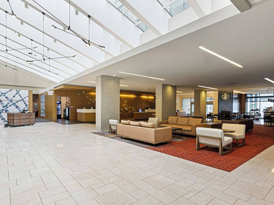 A spacious lobby with a high ceiling, a reception desk, a seating area with sofas and chairs, and a patterned wall.