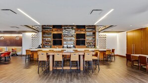 Un espace bar moderne avec un long comptoir, de nombreux tabourets et une variété de bouteilles exposées sur des étagères.