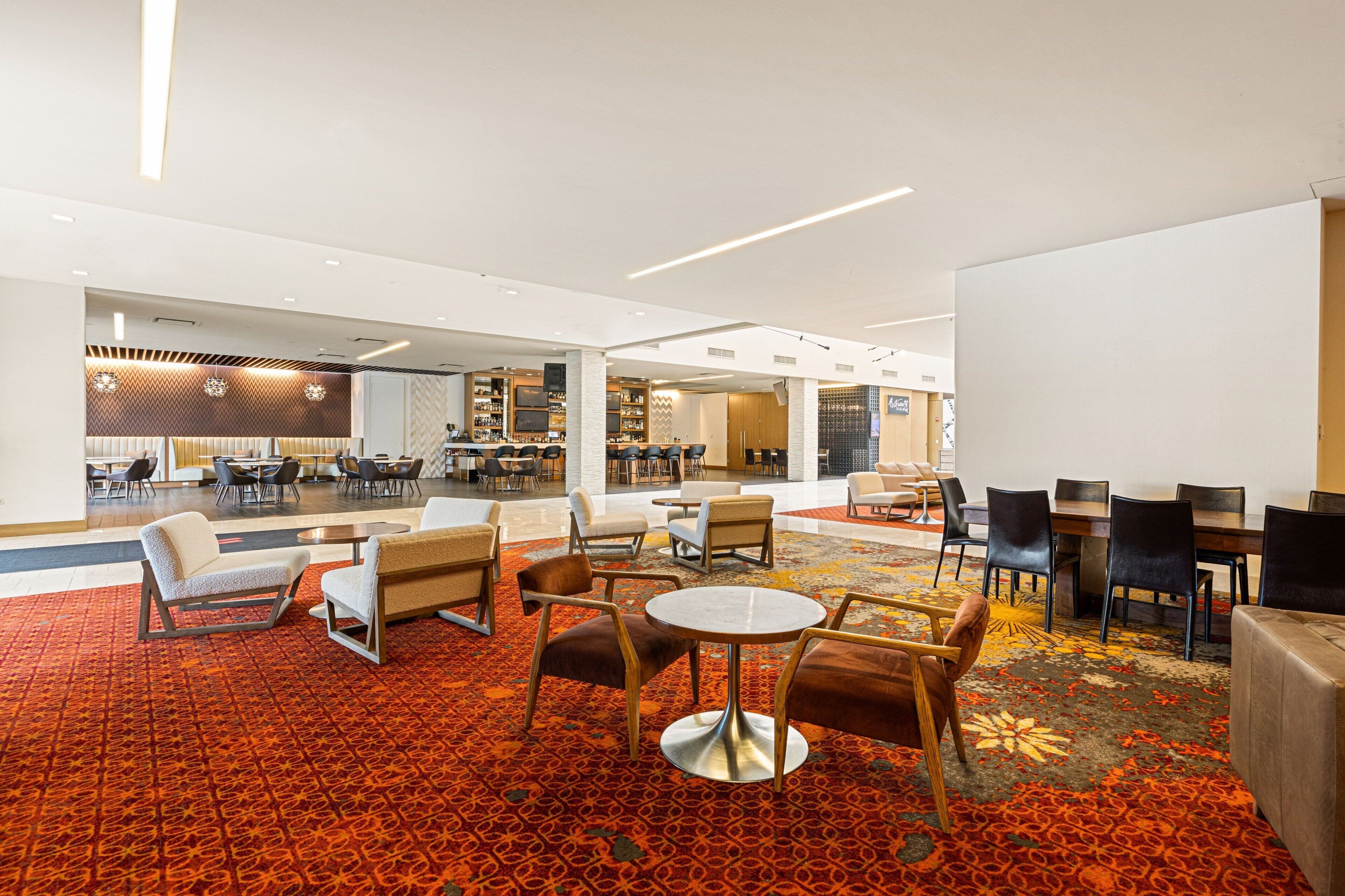 A spacious lobby with a patterned carpet, multiple seating areas including sofas and chairs, and a dining area with tables and chairs.