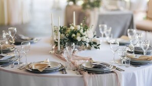 Une table ronde dressée pour un événement formel, avec de la vaisselle en verre transparent, des assiettes et des couverts élégants.