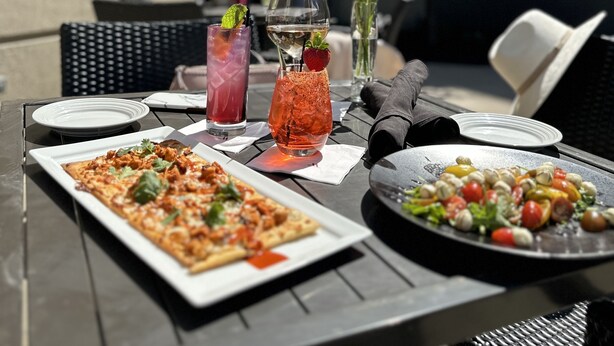 Une table à manger en plein air, avec une pizza, une salade et des boissons.