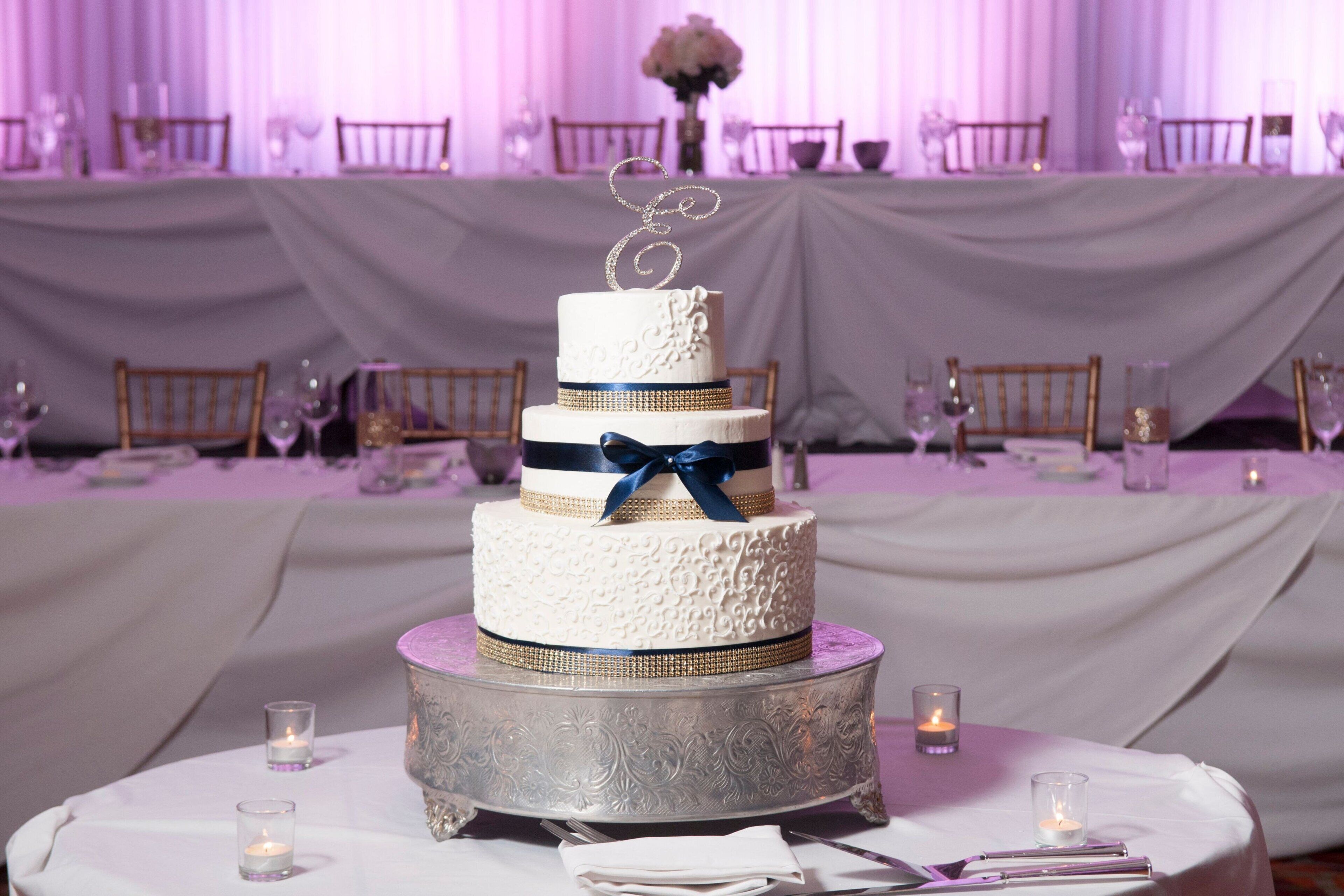 Un pastel de bodas de varios niveles con un adorno decorativo sobre una mesa redonda, rodeado de velas y copas.