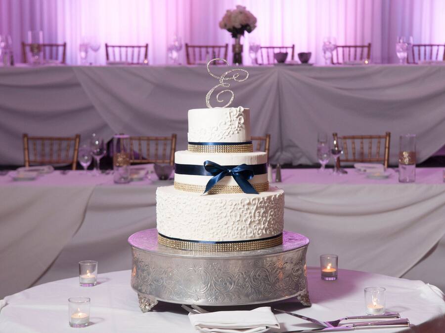 Un pastel de bodas de varios niveles con un adorno decorativo sobre una mesa redonda, rodeado de velas y copas.