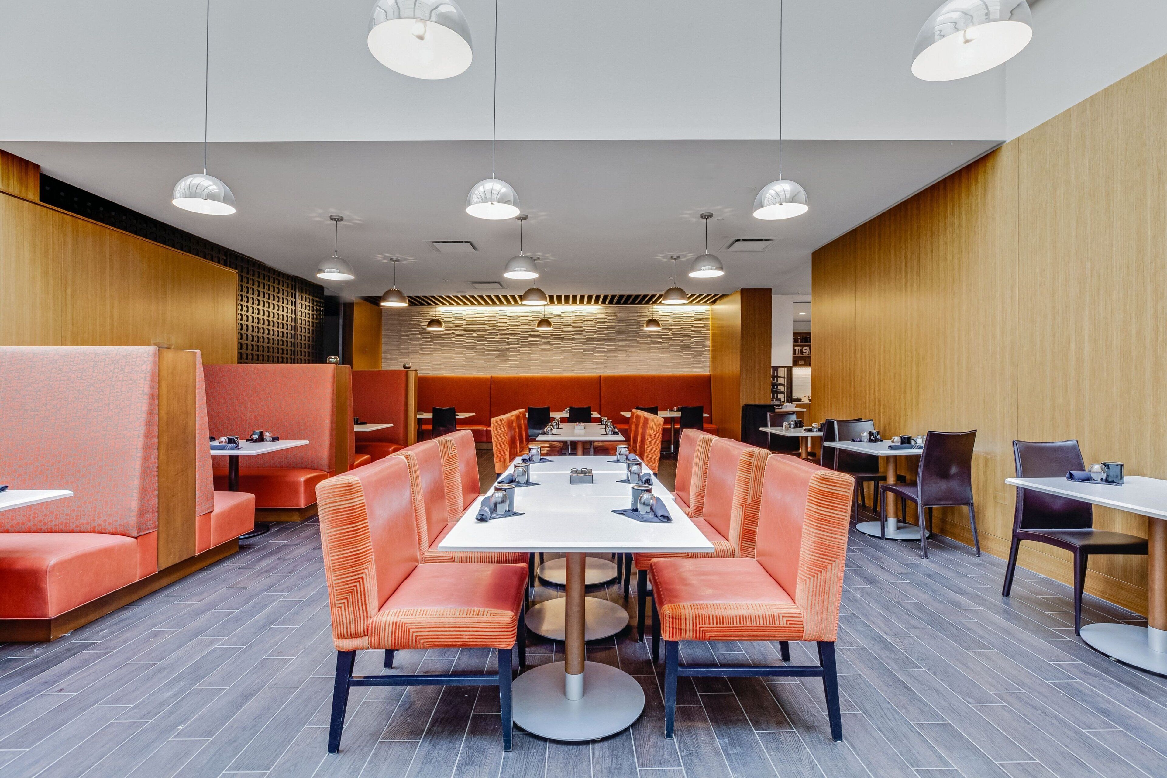 A modern dining area with a long table surrounded by orange booths and individual tables.