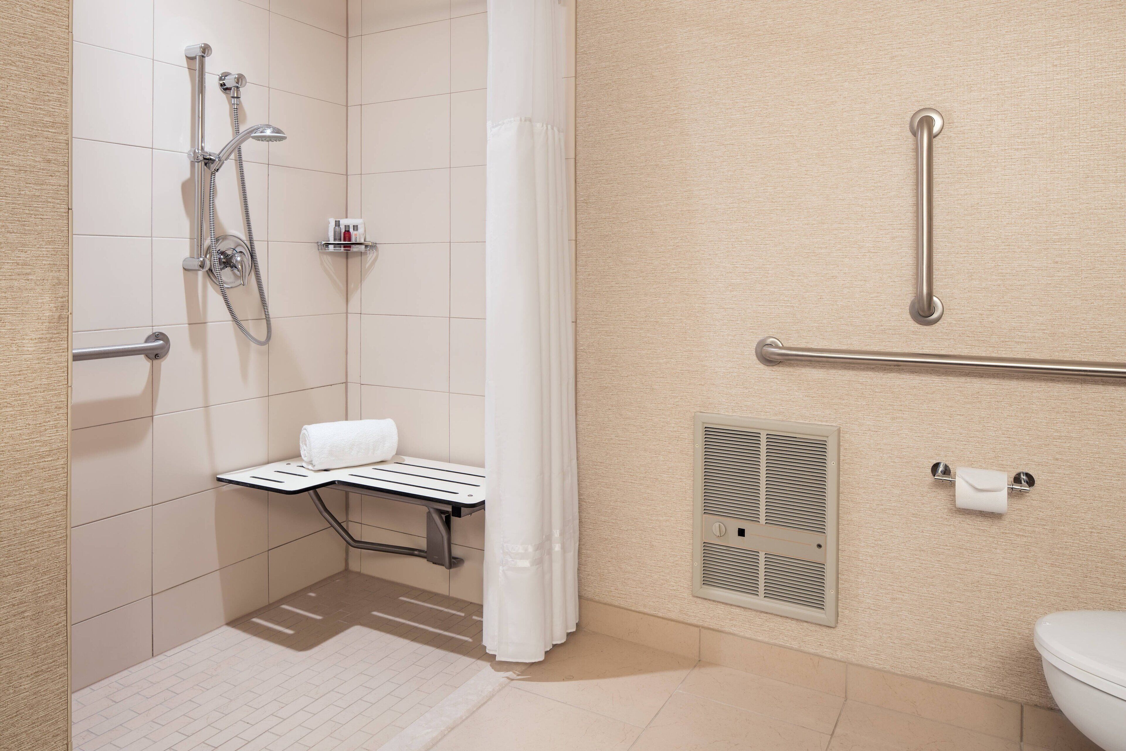 A bathroom with a shower, grab bars, a toilet, and a towel rack.