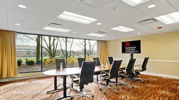A conference room with a large table, multiple chairs, and a view of trees and buildings outside.