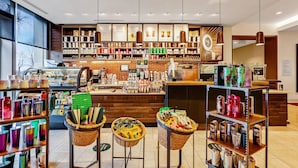 L’intérieur d’un café présente des étagères remplies de grains de café, un comptoir avec un menu, et des paniers remplis de divers articles placés sur des tabourets.