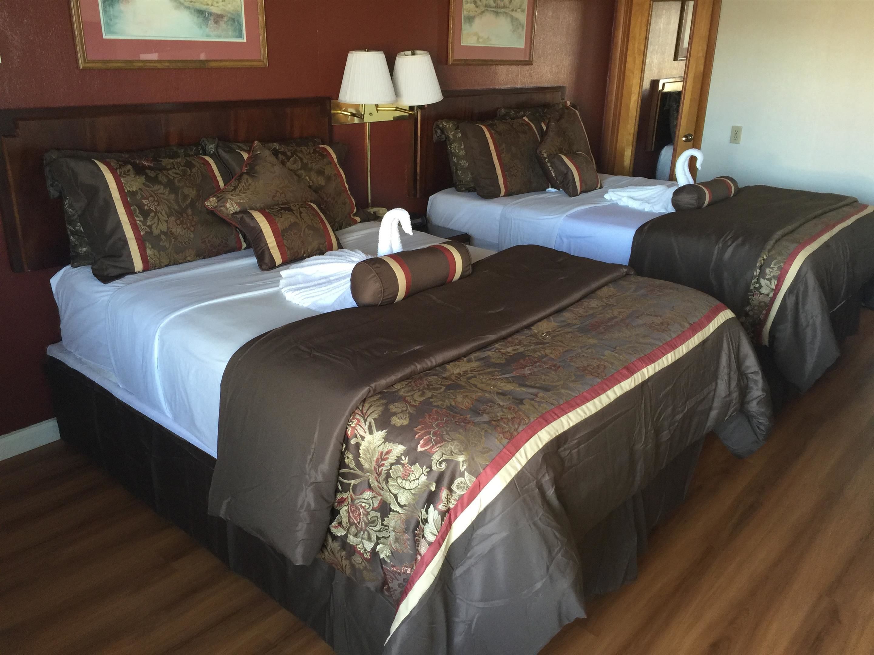 A hotel room with two beds, each with a brown bedspread and matching pillows. There is a nightstand with a lamp between the beds.