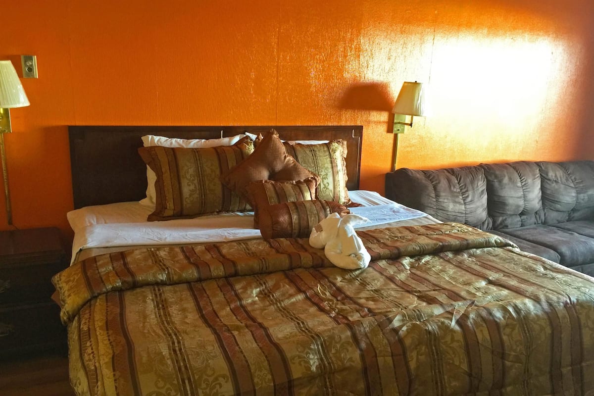 A hotel room with a large bed, multiple pillows, a sofa, and two lamps.