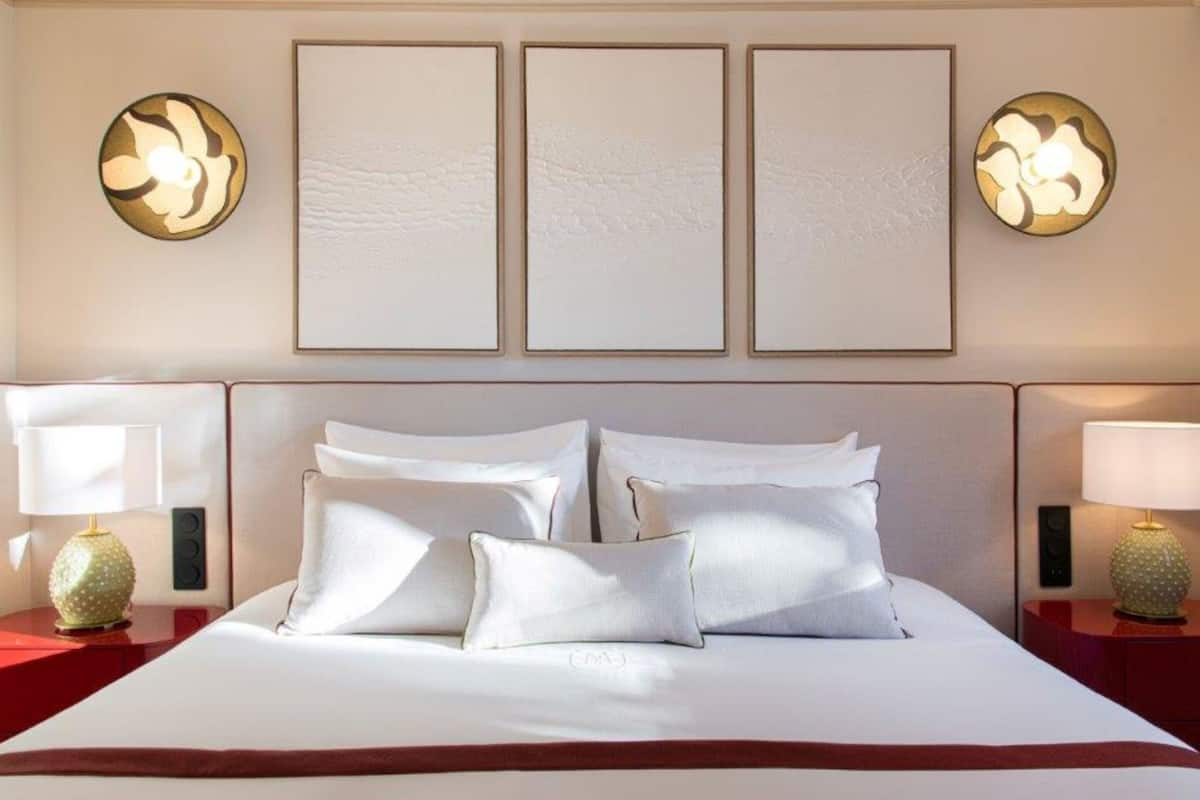 A hotel room with a large bed, two bedside tables, and three framed artworks on the wall.