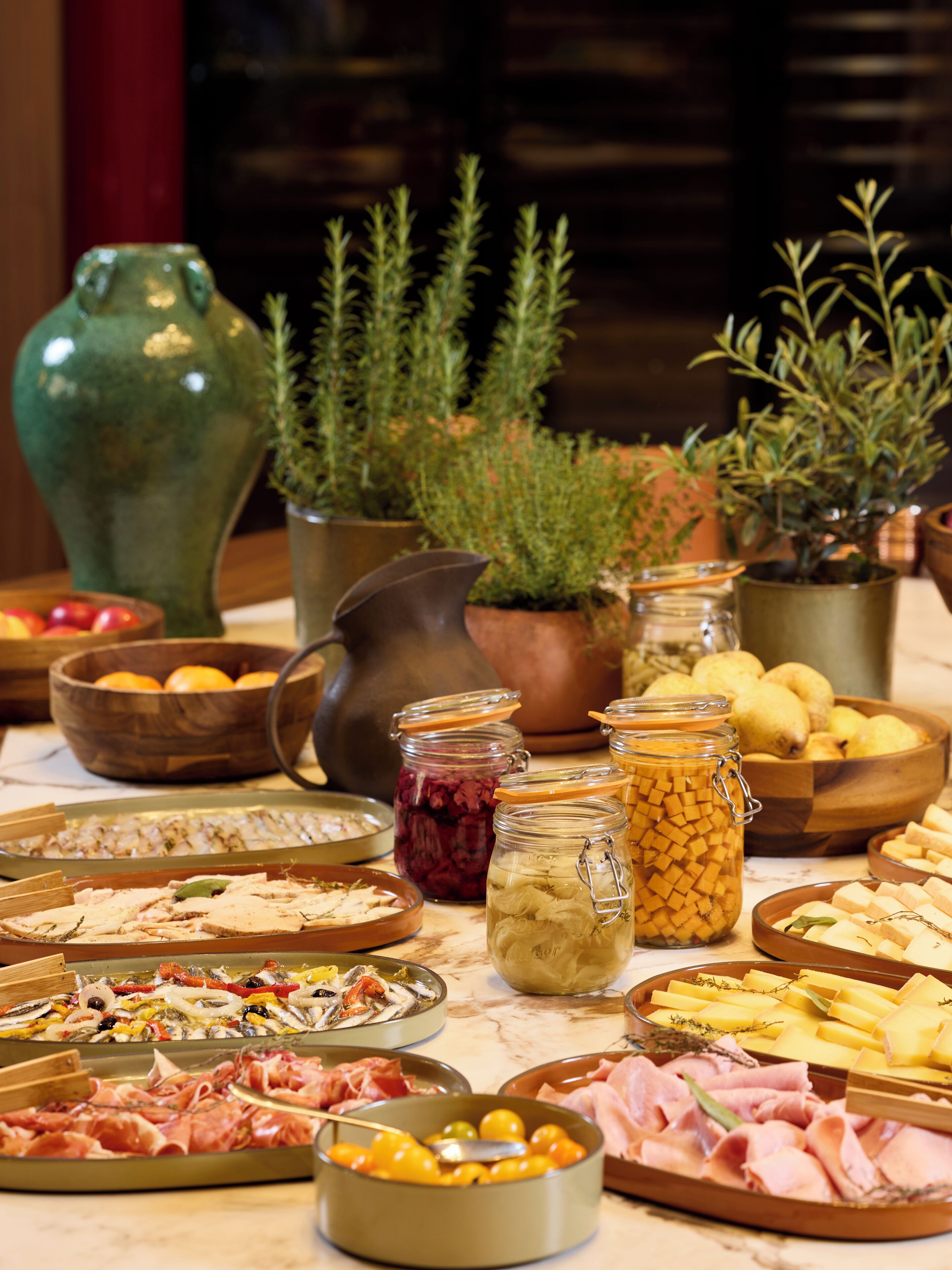 Una mesa con diversos alimentos, entre ellos carnes, quesos y frutas, dispuesta para un bufé.