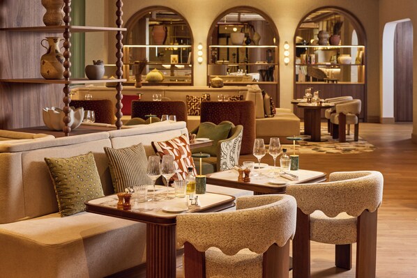 A hotel lobby with a sofa, chairs, tables, and a decorative shelf.