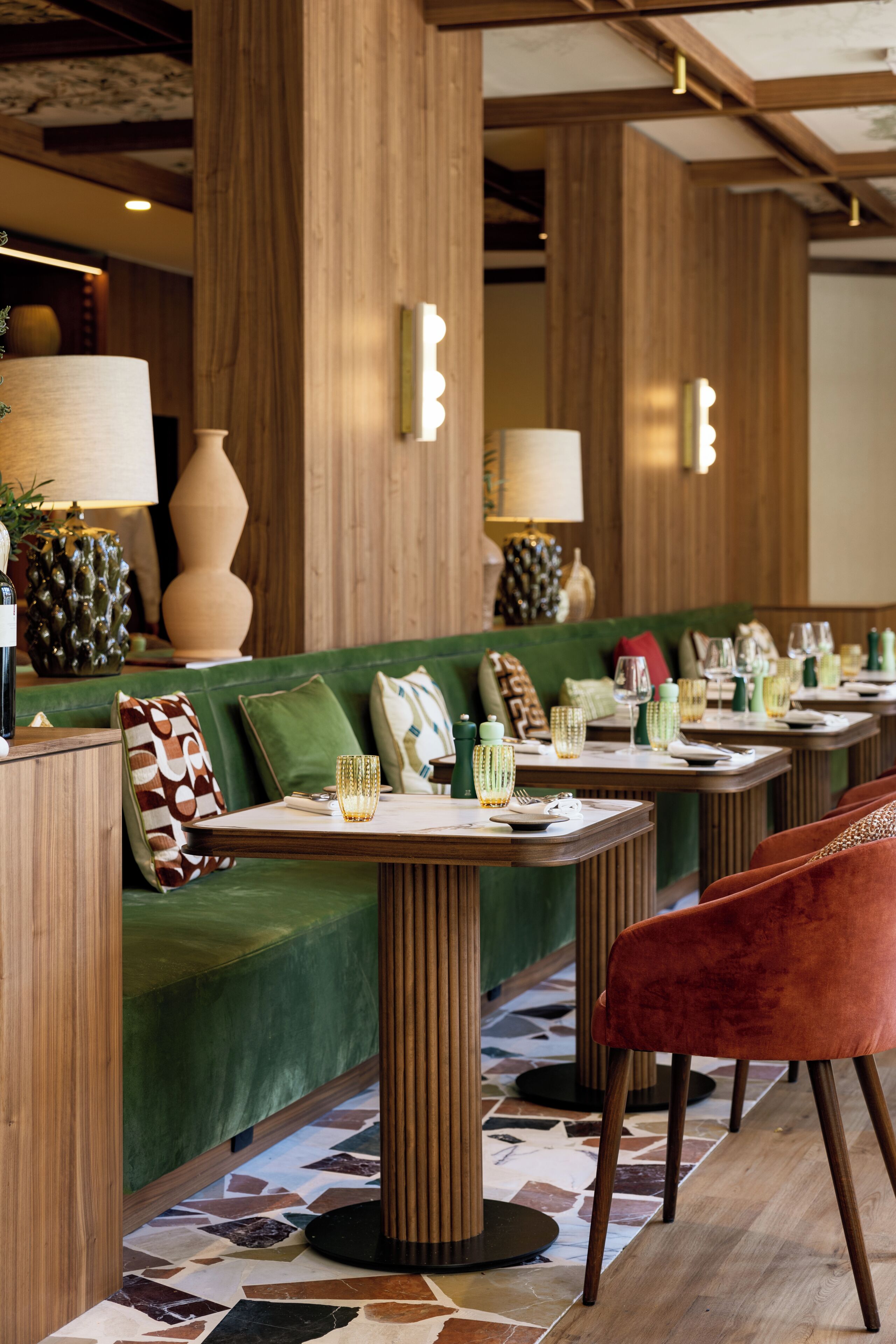 Un restaurante con un sofá verde, columnas de madera y suelo de baldosas.