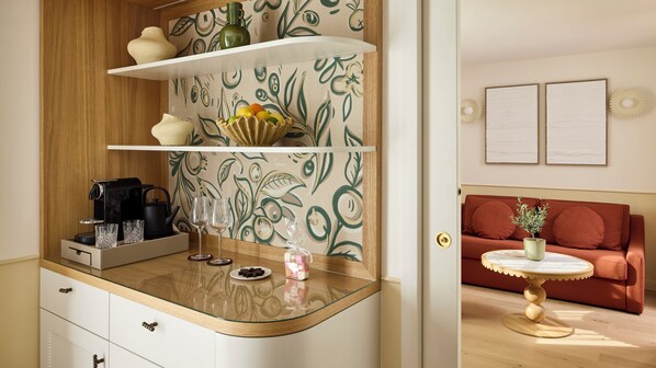 A modern kitchen with a coffee machine, wine glasses, and a fruit bowl on a glass-top counter. - Grand Hôtel Roi René Aix - MGallery Collection (Aix-en-Provence)