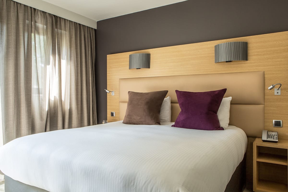 A hotel room with a large bed, two wall-mounted lamps, a bedside telephone, and a wooden headboard.