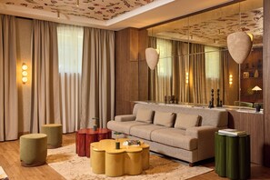 A modern living room with a sofa, round coffee tables, a mirror, and a patterned ceiling. - Grand Hôtel Roi René Aix - MGallery Collection (Aix-en-Provence)
