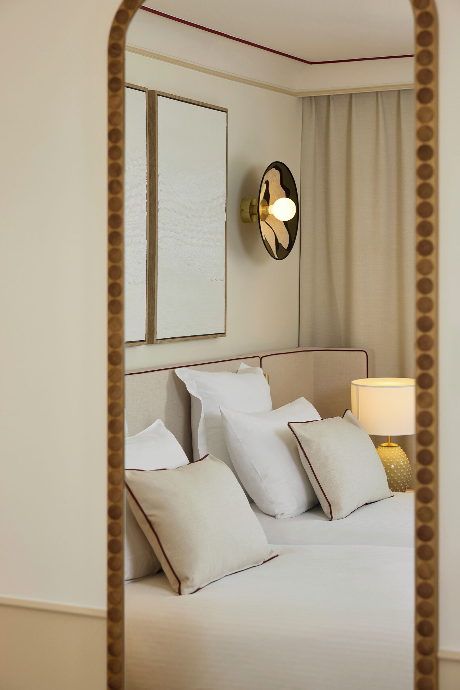 Una habitación de hotel con una cama, almohadas, una lámpara fijada a la pared y un cuadro enmarcado.