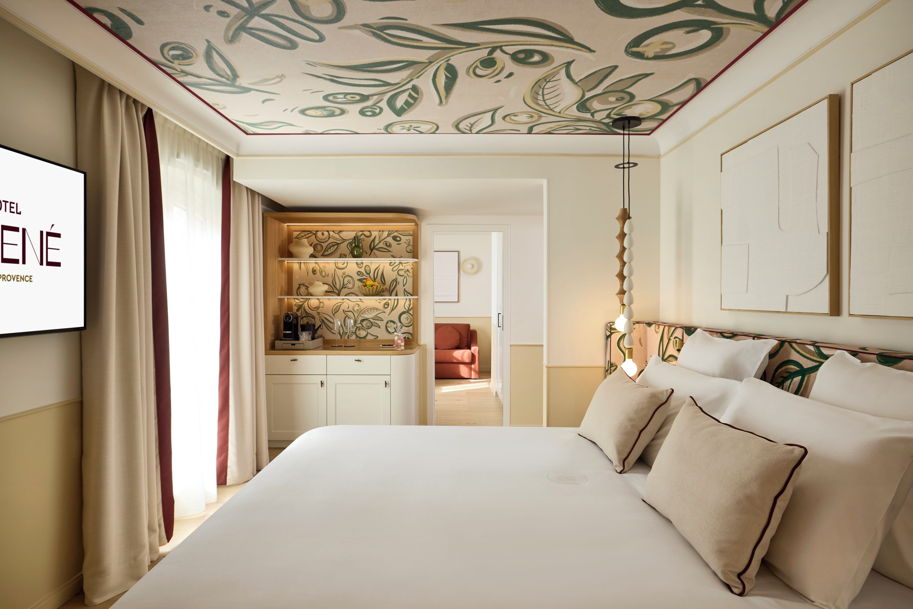 A hotel room with a bed, a TV, a desk with a patterned cabinet, and a red chair.