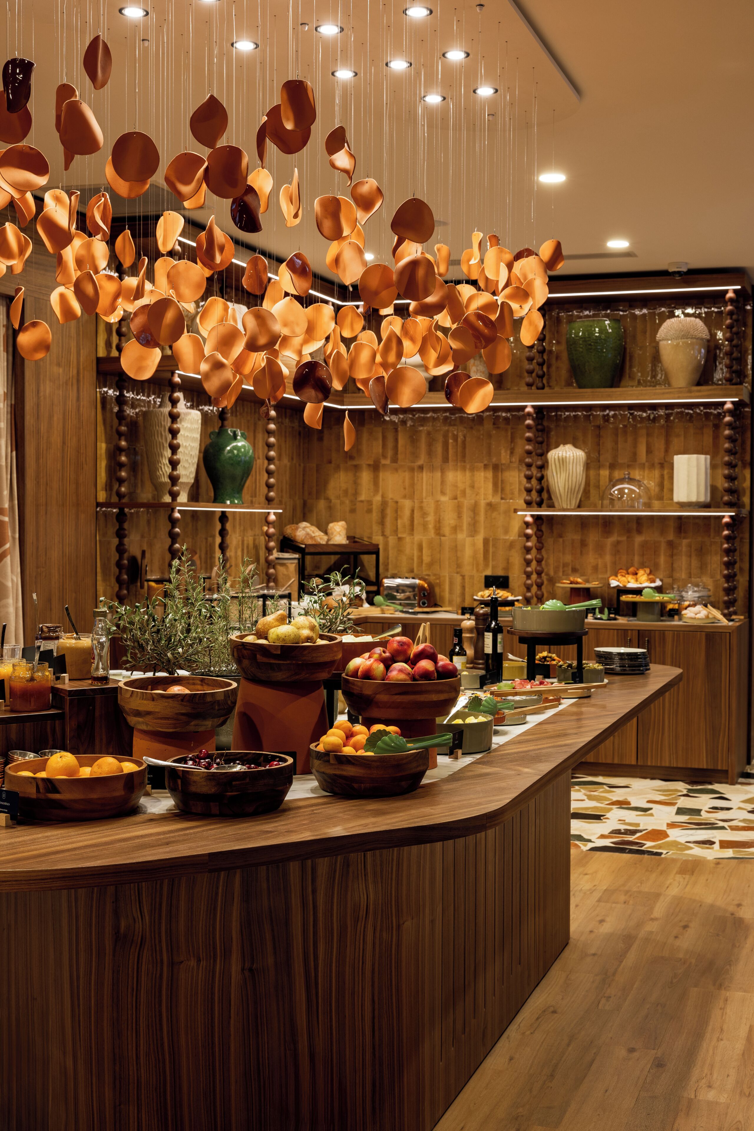Un mostrador de recepción de madera con varios cuencos de frutas y verduras, un florero verde y cerámica colgante.