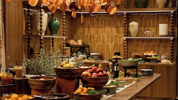 Un mostrador de recepción de madera con varios cuencos de frutas y verduras, un florero verde y cerámica colgante.