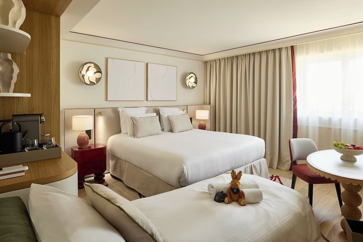 A hotel room with a large bed, two bedside tables, a desk, a chair, and a small table with fruit.