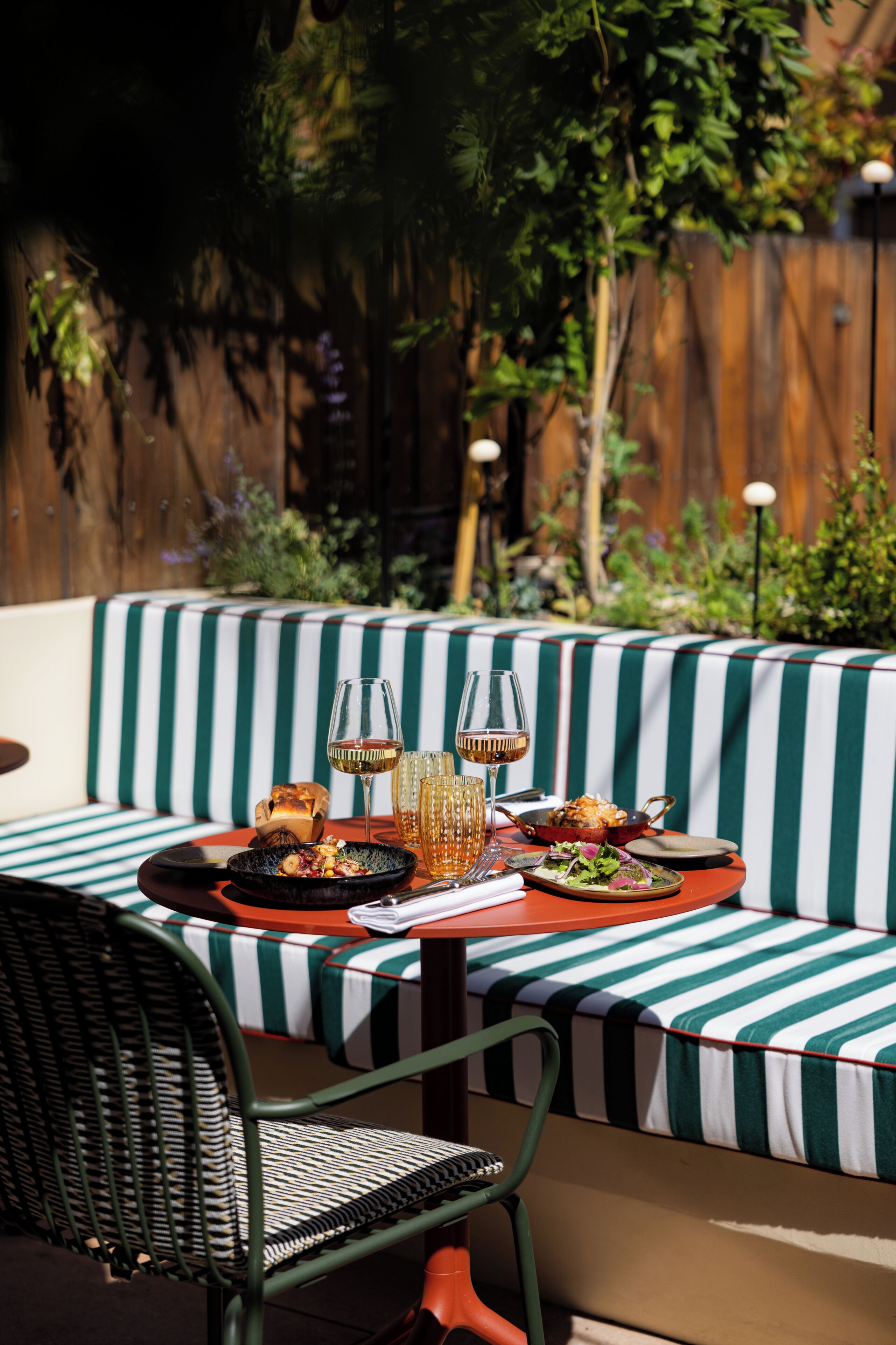A dining area with a striped tablecloth, a wicker chair, and a wooden fence in the background.
