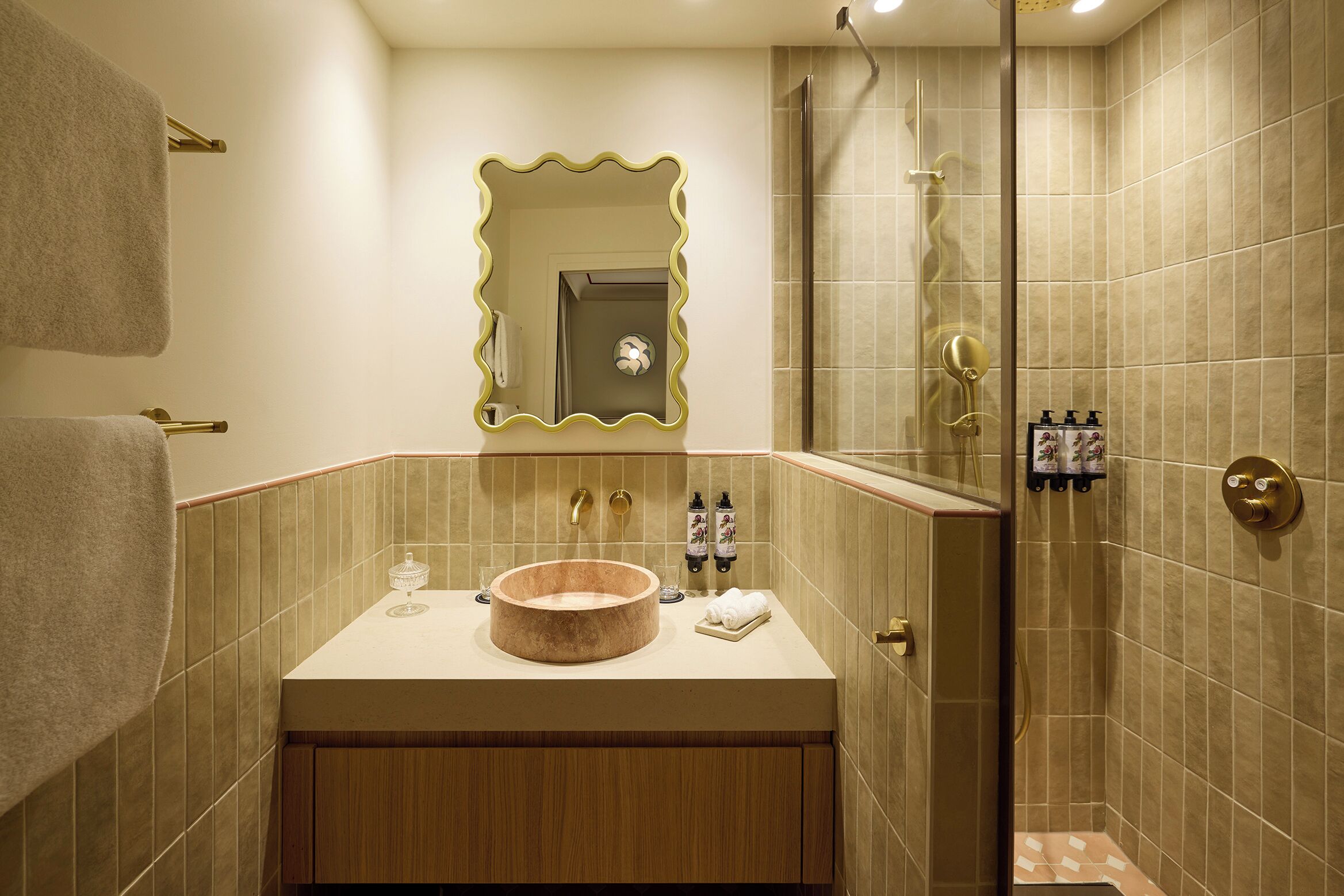 Un baño con un lavabo redondo, un espejo, una ducha y un toallero.