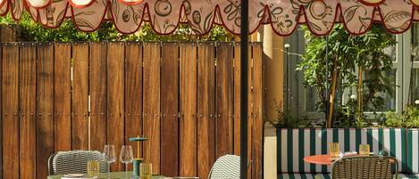 An outdoor seating area with wicker chairs and tables, a wooden fence, and a striped bench.