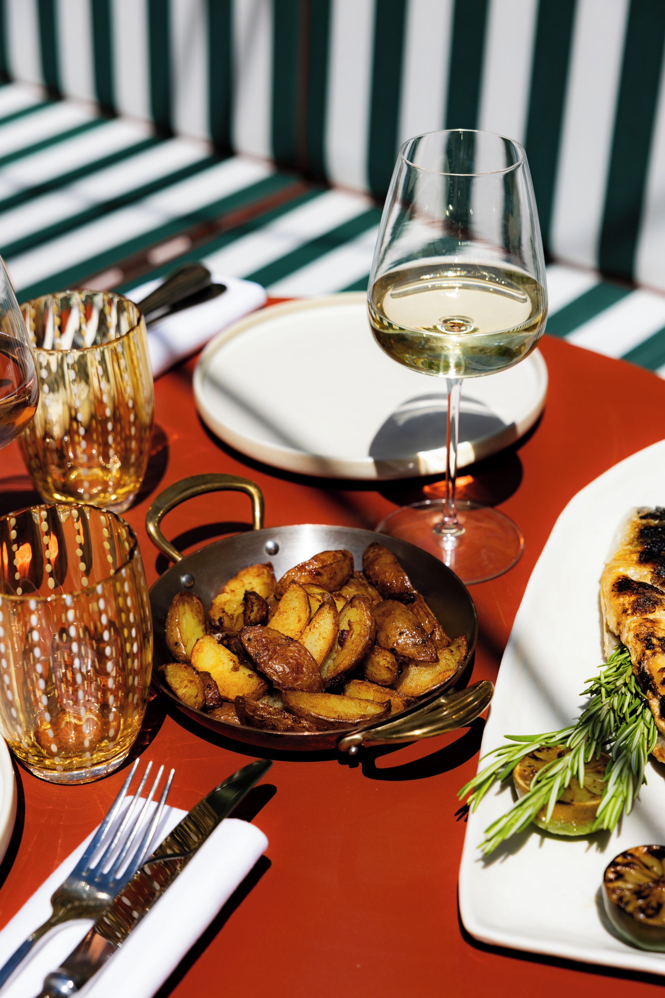 A dining table with a plate of roasted potatoes, a glass of white wine, and a glass of rosé wine.