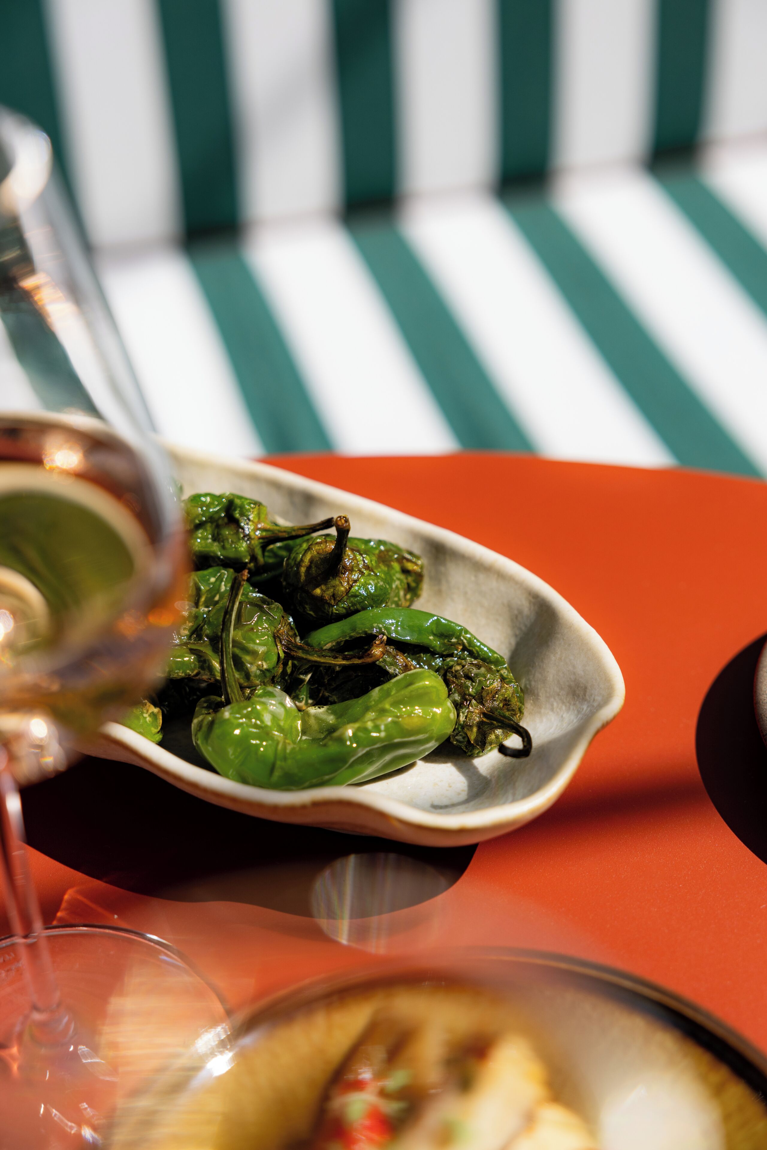 Un plato de pimientos verdes sobre una mesa, con una copa de vino y un bol de comida.