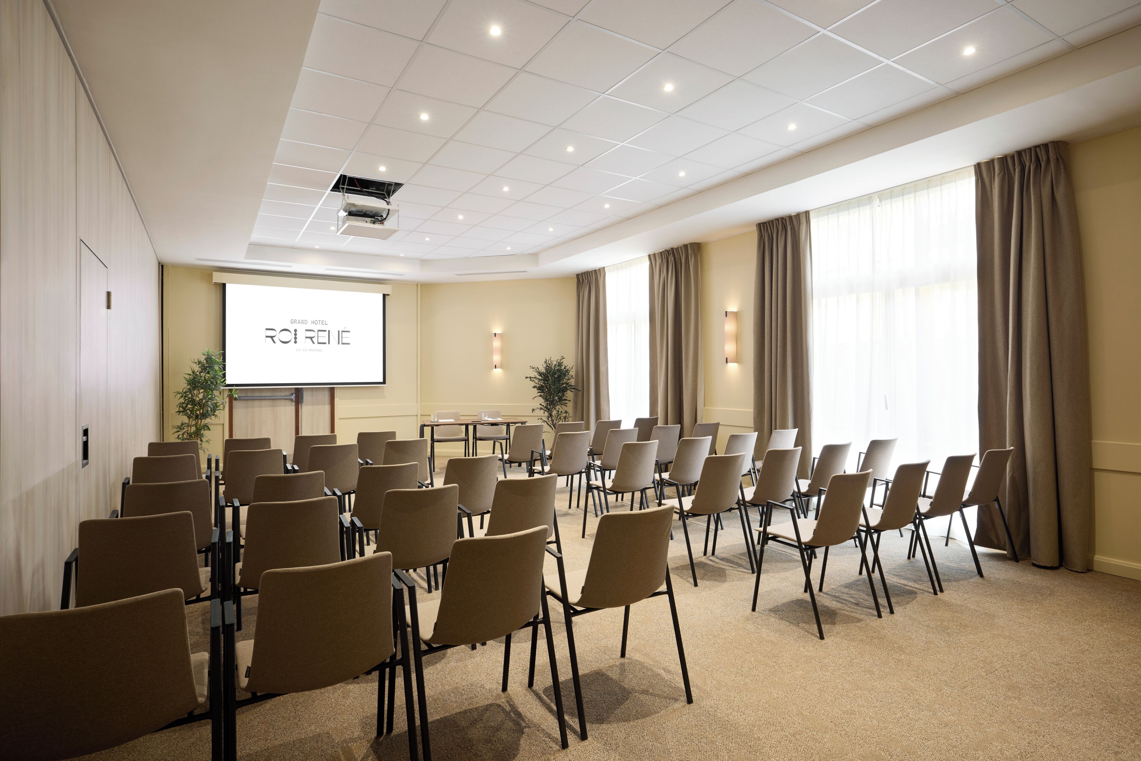 A conference room with rows of chairs, a projector screen, and a large window with curtains.
