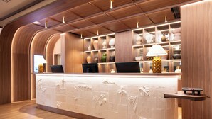 A reception desk with a wooden finish, a white tiled counter, and shelves with decorative items. - Grand Hôtel Roi René Aix - MGallery Collection (Aix-en-Provence)