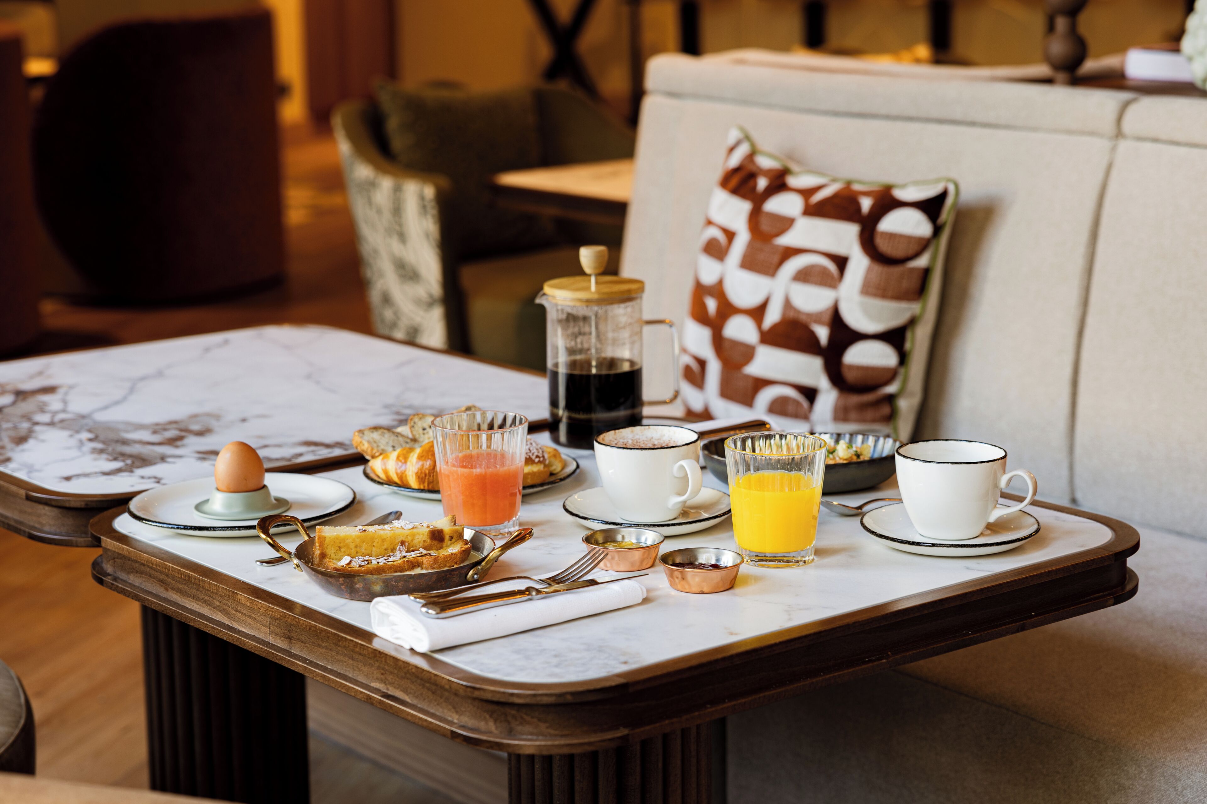 A breakfast table with various breakfast items, a coffee pot, and a cup of coffee.