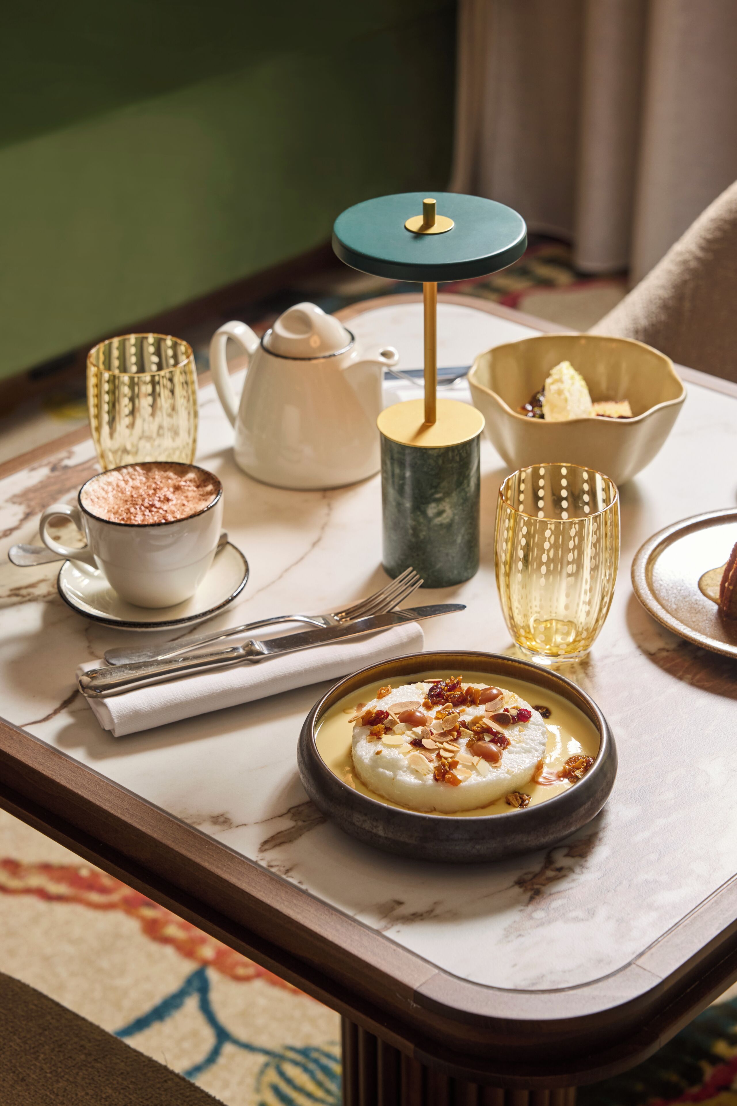 A tray with a dessert, a teapot, a cup, a bowl, and a glass on a marble table.