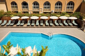 A pool area with lounge chairs and umbrellas, a pool with a ladder, and a building with arched windows in the background. - Grand Hôtel Roi René Aix - MGallery Collection (Aix-en-Provence)