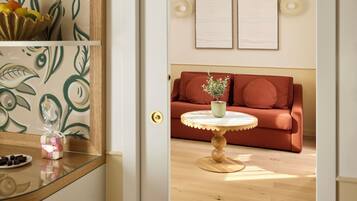 A room with a wooden floor, a round table with a green plant, a red sofa, and a wall with two framed items.