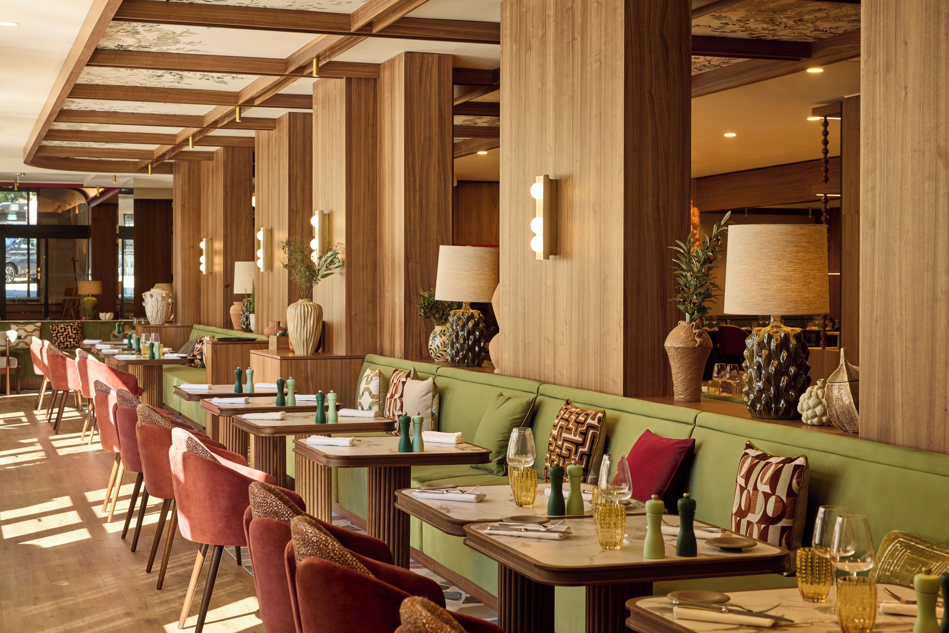 Un restaurant avec des boiseries, des sièges rembourrés de couleur verte et de nombreuses tables accompagnées de chaises.