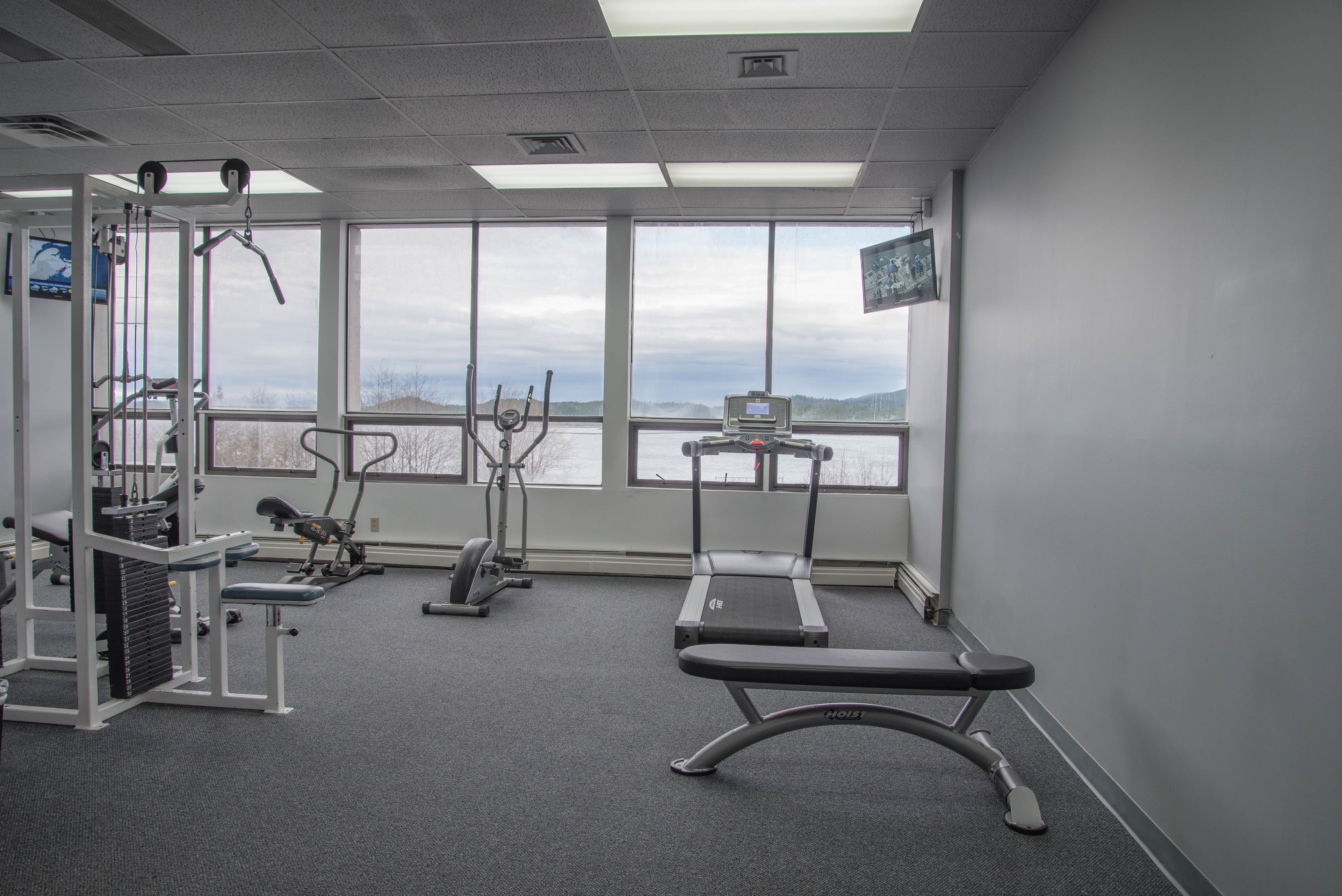 Un gimnasio con equipo de ejercicio, ventanas amplias y vistas al exterior.