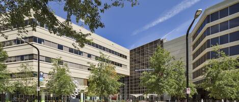 A modern building with multiple floors, outdoor seating area, and trees.