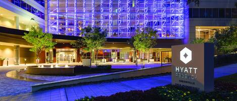 A Hyatt Regency building with a modern facade, a landscaped entrance area, and a sign indicating the location.